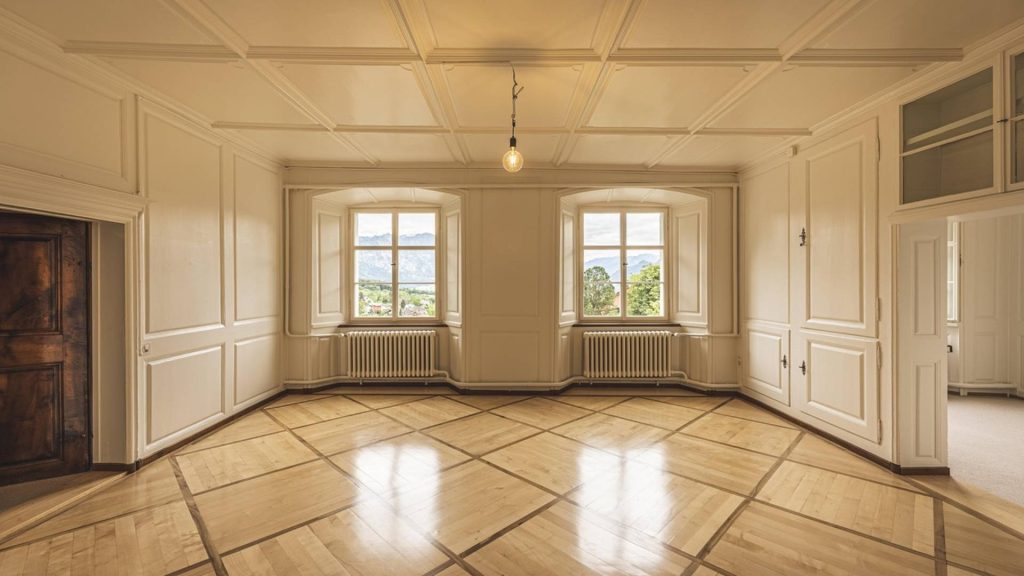 Pièce vide aux boiseries et au plafond à caissons peints en blanc cassé, parquet clair remis en état