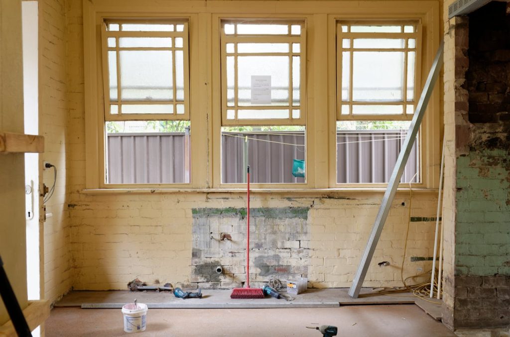 Pièce mise à nu, briques apparentes sous d'anciennes couches de peinture, outils et balai posés au sol