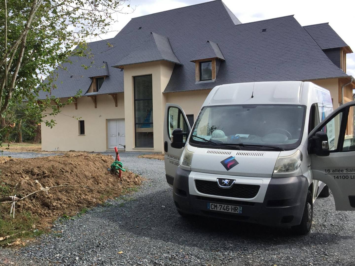 Camion blanc de l'entreprise, portière ouverte, garé sur le gravier devant une maison normande au toit d'ardoise