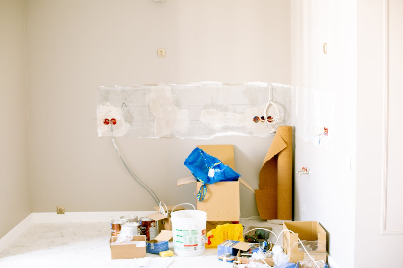 Pièce en travaux, saignées rebouchées au plâtre et fils électriques apparents, pots de peinture et cartons posés sur une bâche